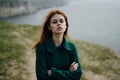 Young woman with long hair in a coat on a cliff of a mountain by the sea, wind, portrait, nature Royalty Free Stock Photo