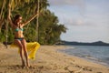 Young woman with long hair, in bikini sitting on rope swing on tropical sunny sandy beach. Palm trees, blue sky and sea Royalty Free Stock Photo