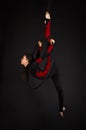 A young woman with long hair doing aerial acrobatics in a black and red suit, performs exercises in the air ring Royalty Free Stock Photo