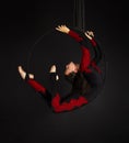 A young woman with long hair doing aerial acrobatics in a black and red suit, performs exercises in the air ring Royalty Free Stock Photo