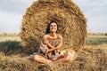 A young woman with long hair and in a dress sits near a hay bale. Woman posing smiling and looking at camera Royalty Free Stock Photo