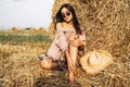 A young woman with long hair and in a dress sits near a hay bale. Woman posing smiling and looking at camera Royalty Free Stock Photo