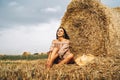 A young woman with long hair and in a dress sits near a hay bale. Woman posing smiling and looking at camera Royalty Free Stock Photo