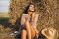 A young woman with long hair and in a dress sits near a hay bale. Woman posing smiling and looking at camera Royalty Free Stock Photo