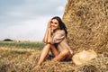 A young woman with long hair and in a dress sits near a hay bale. Woman posing smiling and looking at camera Royalty Free Stock Photo