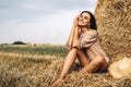 A young woman with long hair and in a dress sits near a hay bale. Woman posing smiling and looking at camera Royalty Free Stock Photo