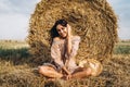 A young woman with long hair and in a dress sits near a hay bale. Woman posing smiling and looking at camera Royalty Free Stock Photo