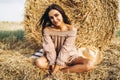 A young woman with long hair and in a dress sits near a hay bale. Woman posing smiling and looking at camera Royalty Free Stock Photo