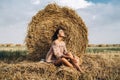 A young woman with long hair and in a dress sits near a hay bale. Woman posing smiling and looking at camera Royalty Free Stock Photo