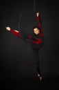 A young woman with long hair is engaged in aerial acrobatics in a black-and-red suit, performs exercises in an aerial ring in a Royalty Free Stock Photo