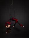 A young woman with long hair is engaged in aerial acrobatics in a black-and-red suit, performs exercises in an aerial ring in a Royalty Free Stock Photo