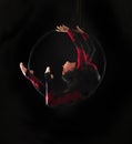 A young woman with long hair is engaged in aerial acrobatics in a black-and-red suit, performs exercises in an aerial ring in a Royalty Free Stock Photo