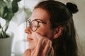 Woman in eyeglasses doing face lifting massage with gua sha in front of a mirror