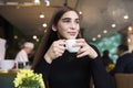 Young woman with long hair feel lonely, dreaming, drinking coffee in hands having rest in cafe near window