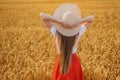 Young woman with long hair in hat on wheat field background. Hands behind head. Rear view Royalty Free Stock Photo