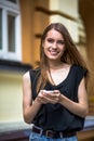 Young woman with long hair holding phone in hands.