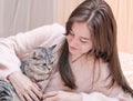 young woman with long hair lying on a bed and grey tabby cat sitting next to her. pet friends, lovely pets. Royalty Free Stock Photo