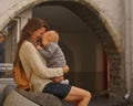 Young woman with long hair sitting on bench and hugging little baby. Baby and mother laughing. Family love and sincerity