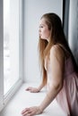 Young woman with long hair standing near window and looking out Royalty Free Stock Photo