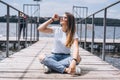 Young woman with long hair in stylish glasses posing on a wooden pier near the lake. Girl dressed in jeans and t-shirt smiling and Royalty Free Stock Photo