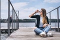 Young woman with long hair in stylish glasses posing on a wooden pier near the lake. Girl dressed in jeans and t-shirt smiling and Royalty Free Stock Photo