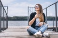 Young woman with long hair in stylish glasses posing on a wooden pier near the lake. Girl dressed in jeans and t-shirt smiling and Royalty Free Stock Photo