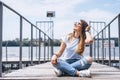 Young woman with long hair in stylish glasses posing on a wooden pier near the lake. Girl dressed in jeans and t-shirt smiling and Royalty Free Stock Photo