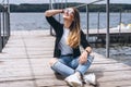 Young woman with long hair in stylish glasses posing on a wooden pier near the lake. Girl dressed in jeans and t-shirt smiling and Royalty Free Stock Photo