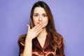 Young woman with long hair wearing brown pajama smiles and is surprised, covering her mouth with her palm Royalty Free Stock Photo