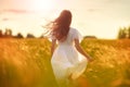 Young woman with long hair in white dress walking in a rye field at the sunset golden hour. Freedom inspiration environment