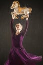 Young woman in purple dress dancing with antique carousel horse. Royalty Free Stock Photo