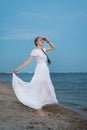 Young woman in long white dress stands on shore of sea background. Vertical frame Royalty Free Stock Photo