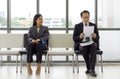 Young woman look and smile at a man sitting further away. Asian business people waiting for job interview by sitting spaced apart Royalty Free Stock Photo