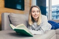 Young woman looking at  camera, lying on sofa at home and reading a book. student girl studying lessons Royalty Free Stock Photo