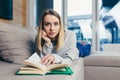 Young woman looking at the camera, lying on sofa at home and reading a book. student girl studying lessons Royalty Free Stock Photo