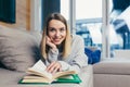 Young woman looking at the camera, lying on sofa at home and reading a book. student girl studying lessons Royalty Free Stock Photo