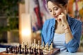 Young woman looking at the chess pieces on the board and thinking about a move while playing chess board game at home Royalty Free Stock Photo