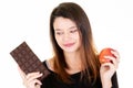 Young woman looking fresh apple while eating chocolate bar