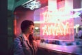 Young woman looking through the glass next to a club with a window with neon lights take away