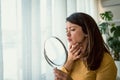 Young woman looking herself in the mirror at home. Worried about acne caused by wearing a mask Royalty Free Stock Photo