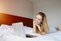 Young woman looking at laptop working home remotely at white bed Royalty Free Stock Photo