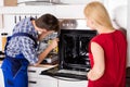 Young Woman Looking At Male Worker Repairing Oven Royalty Free Stock Photo