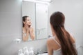 A young woman looking at mirror and examines her skin, touching face with finger Royalty Free Stock Photo