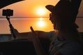 Young woman looking out car window of the sunset on the sea and and photographed on the phone. Royalty Free Stock Photo