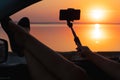 Young woman looking out car window of the sunset on the sea and and photographed on the phone. Royalty Free Stock Photo