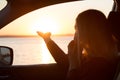 Young woman looking out car window of the sunset on the sea and talking on the phone. Royalty Free Stock Photo