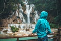 A young woman looks and admires the beautiful waterfall in the wild jungles of Asia.. Blonde Backpacker Or Traveler Girl in a Blue Royalty Free Stock Photo