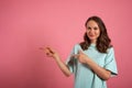 Young woman looks at the camera and pointing somewhere to the side on a pink background Royalty Free Stock Photo