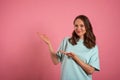 Young woman looks at the camera and pointing somewhere to the side on a pink background Royalty Free Stock Photo