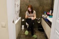 A young woman looks at her phone while sitting on the toilet in the bathroom. Lifestyle photos and casual life Royalty Free Stock Photo